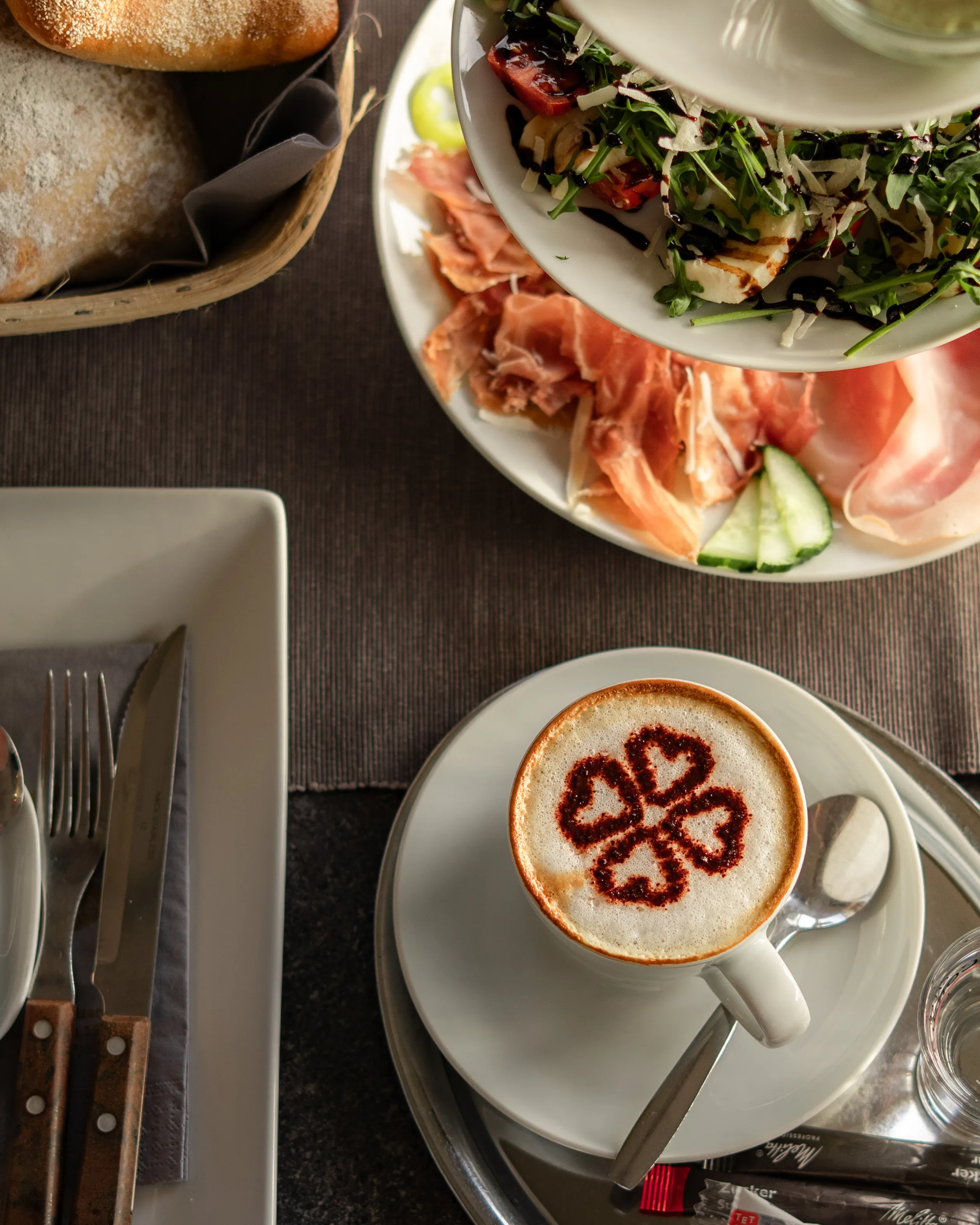 Cappuccino mit Kleeblatt-Latte-Art und Frühstücksteller