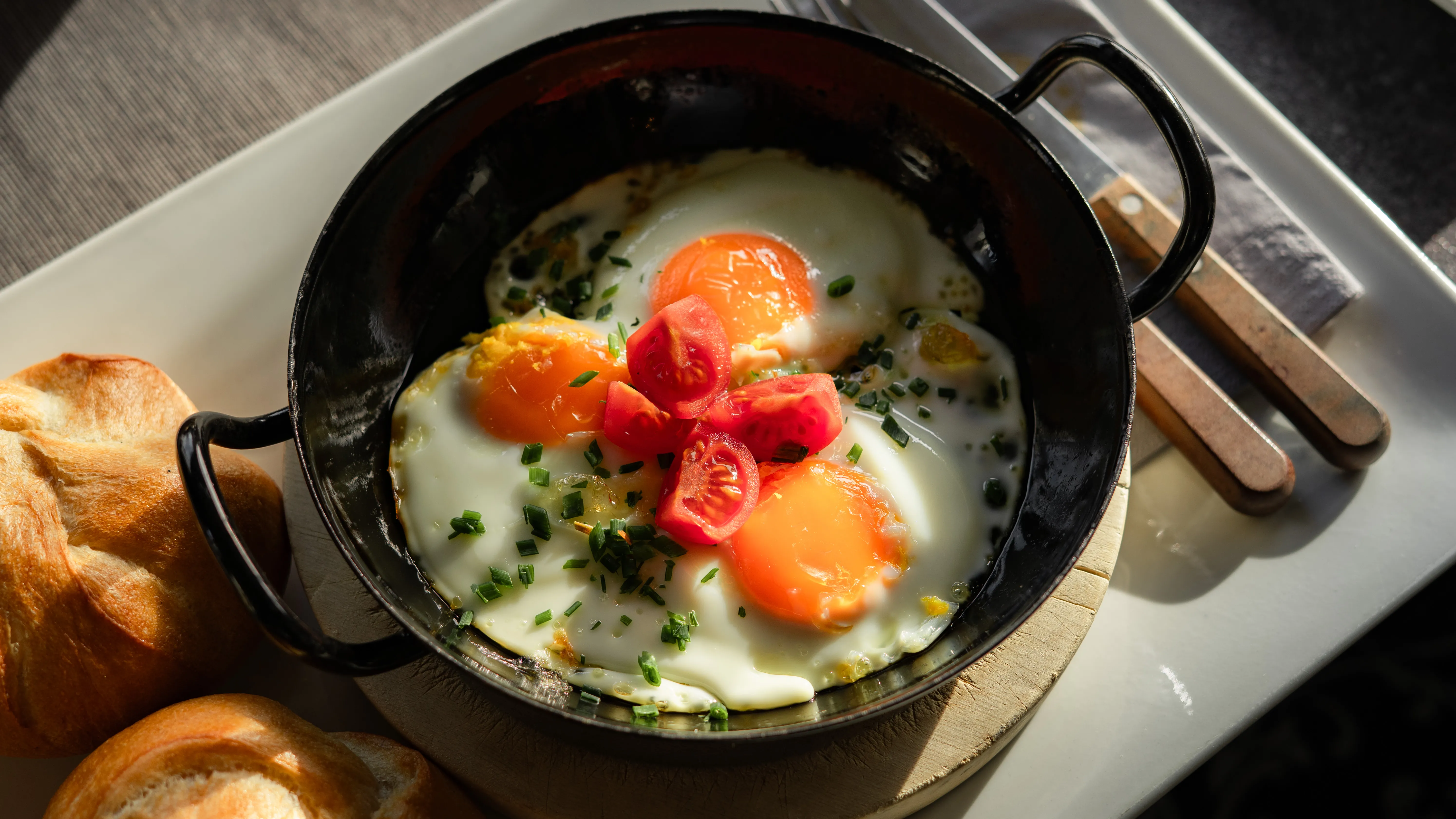 Drei Spiegeleier in einer kleinen Pfanne mit Tomaten und Schnittlauch