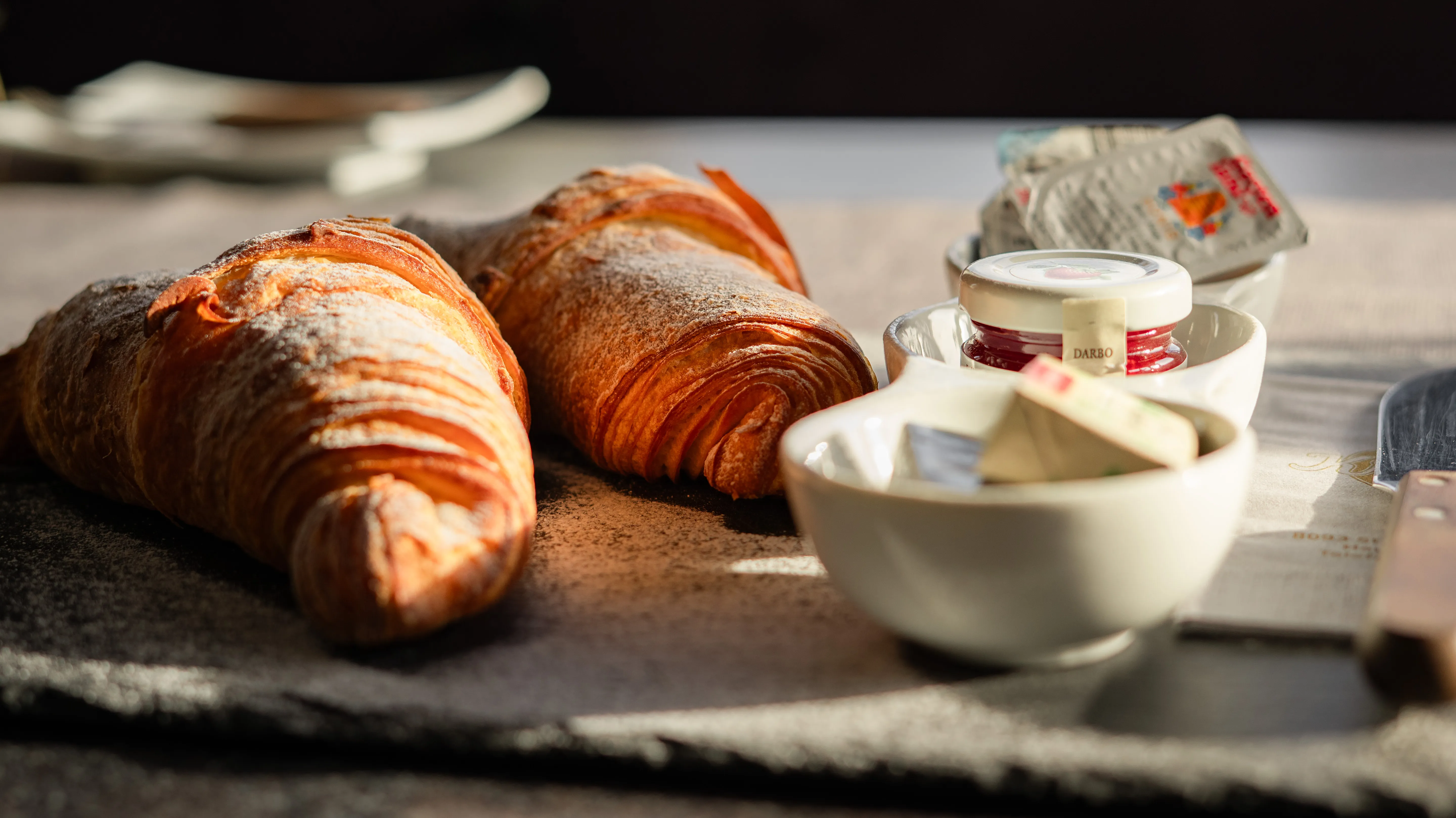 Zwei Croissants auf Steinplatte mit Butter und Marmelade